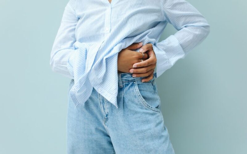 A person in a blue striped shirt and jeans, posing fashionably against a neutral background.