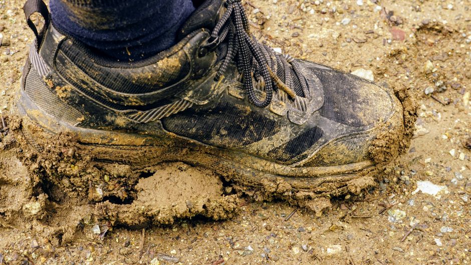 A trekking shoe covered in mud on a dirt path, showcasing outdoor adventure.