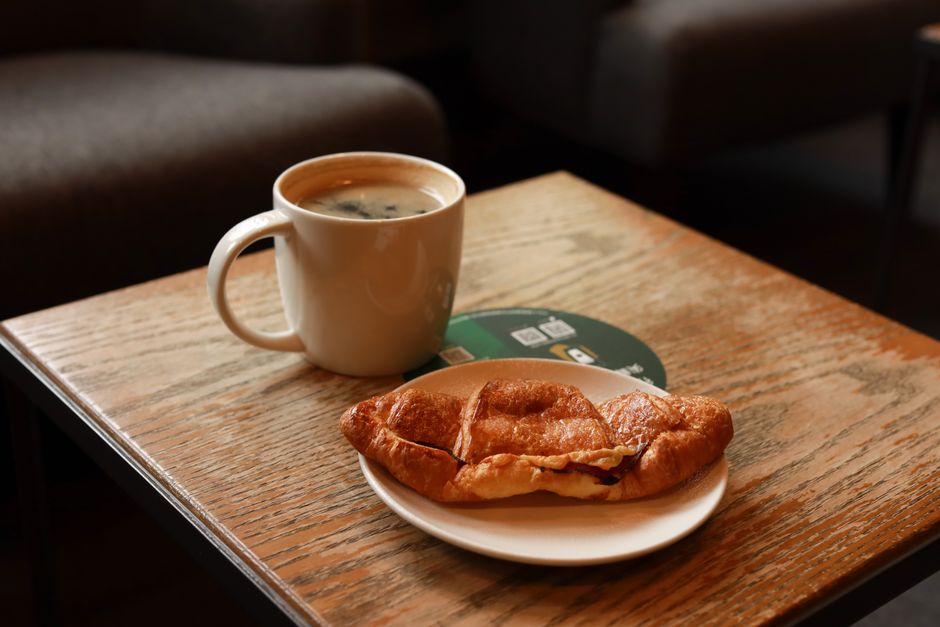 A warm cup of coffee and croissant on a wooden table in a cozy cafe setting.