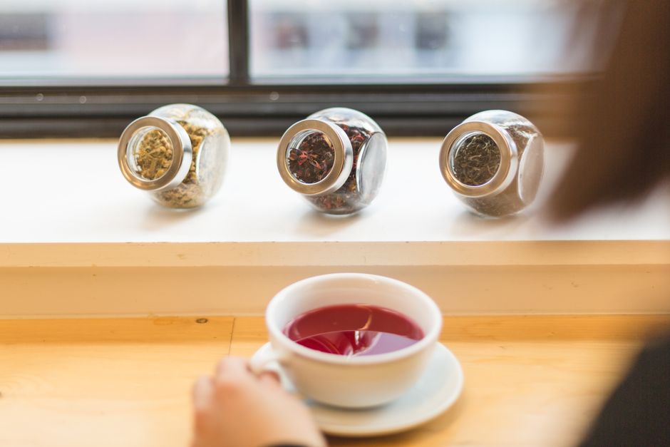 A warm cup of herbal tea with assorted dried herbs in glass jars, creating a cozy and healthy ambiance.