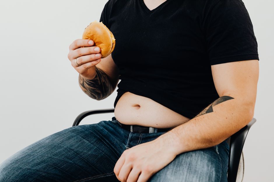 Adult man sitting with a burger. Casual style with tattoos and denim jeans.