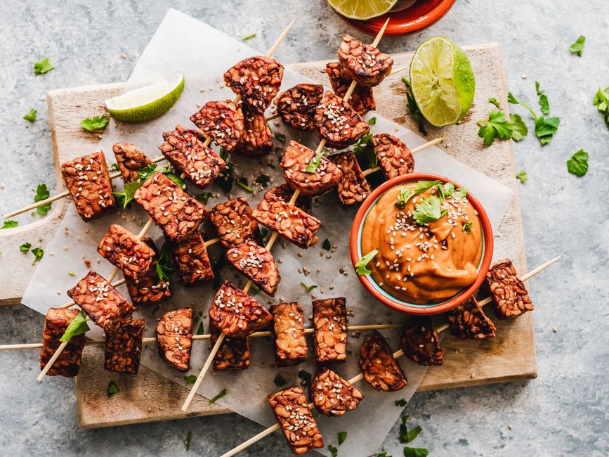 Appetizing grilled tempeh skewers paired with a rich, spicy peanut sauce, garnished with fresh herbs.