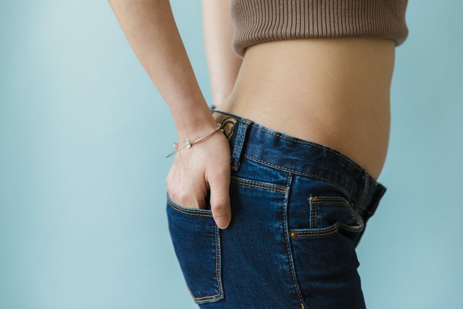 Close-up of a woman's waist in a crop top and blue jeans, hand in pocket, showcasing casual fashion.