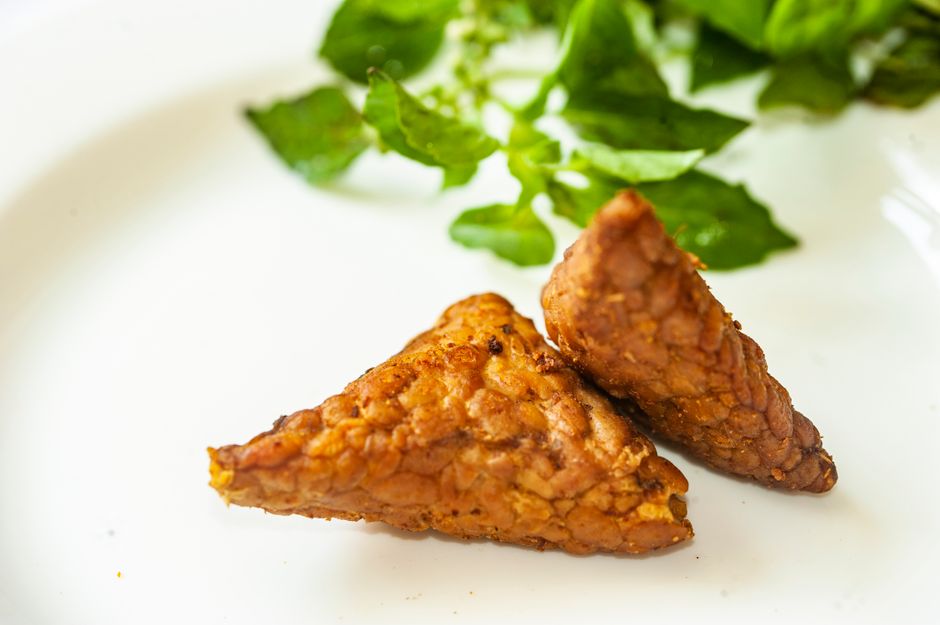 Close-up of crispy fried tempeh served on a plate with fresh herbs.