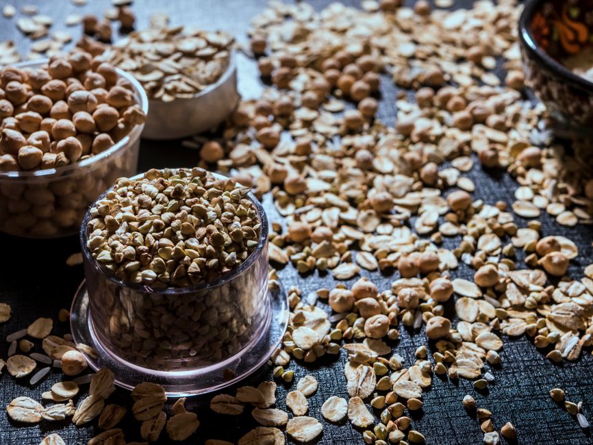 Close-up of diverse grains and legumes in plastic cups on a textured surface, highlighting healthy food options.