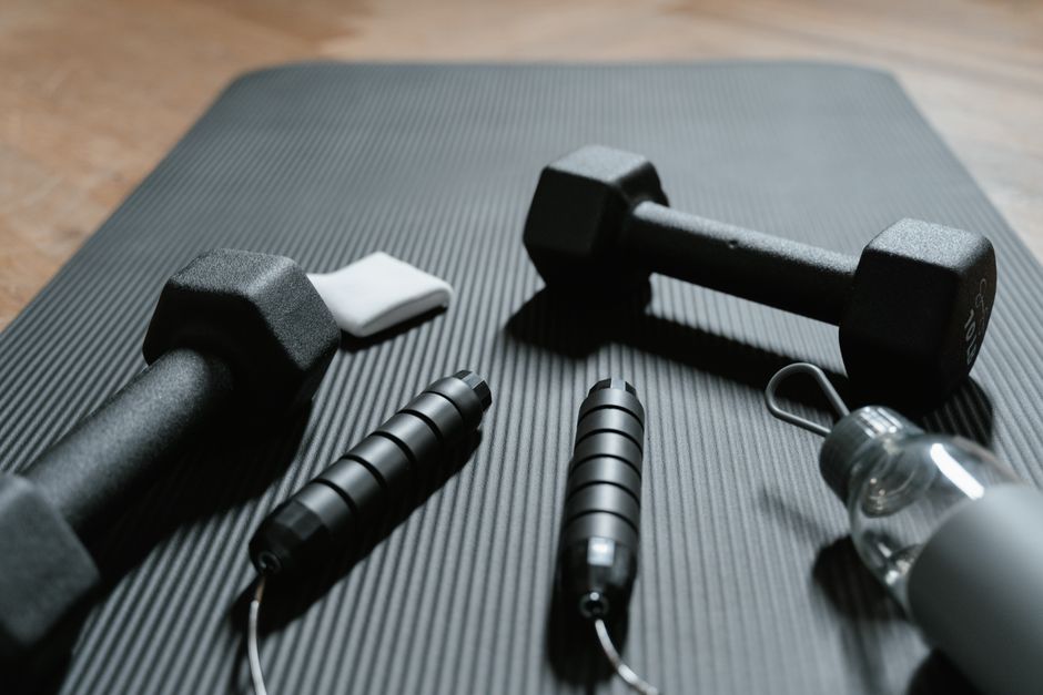 Close-up of dumbbells, jump rope, and water bottle on a yoga mat, ideal for home fitness routines.