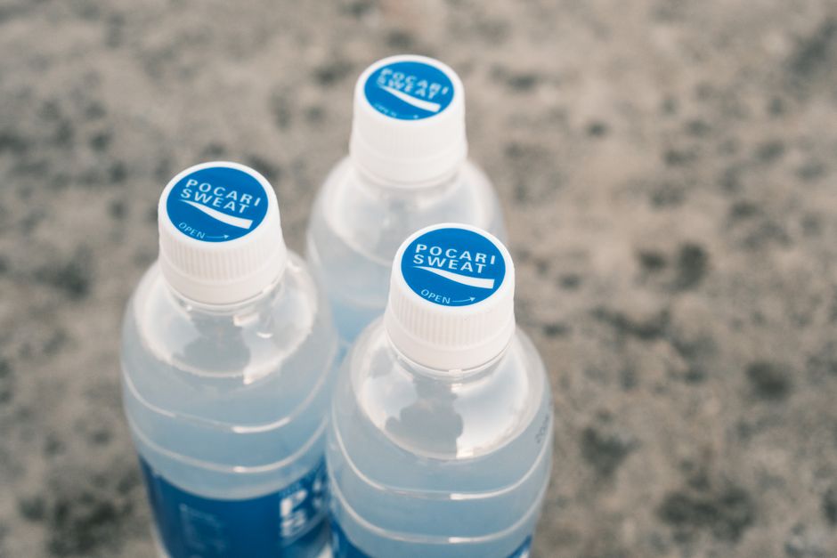 Close-up of three Pocari Sweat bottles arranged on a textured stone surface.