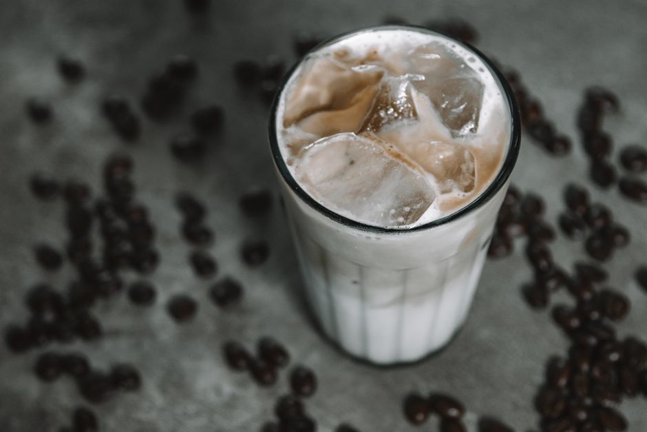 Close-up view of a creamy iced coffee with ice cubes, surrounded by coffee beans.