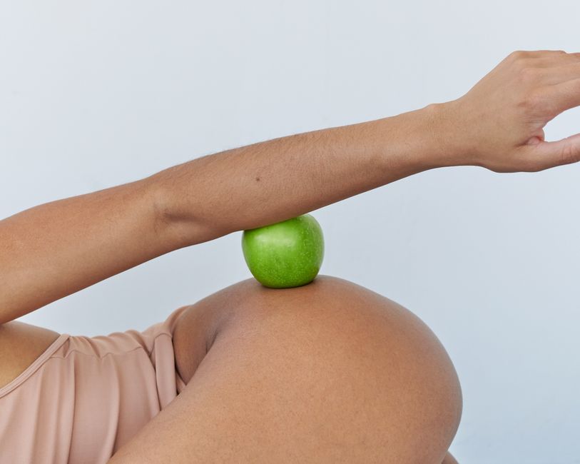 Creative portrayal of pregnancy with a green apple and arm in studio setting.
