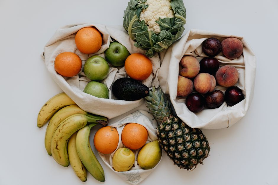 Flat lay of fresh fruits and vegetables including apples, bananas, peaches and more on a white background.