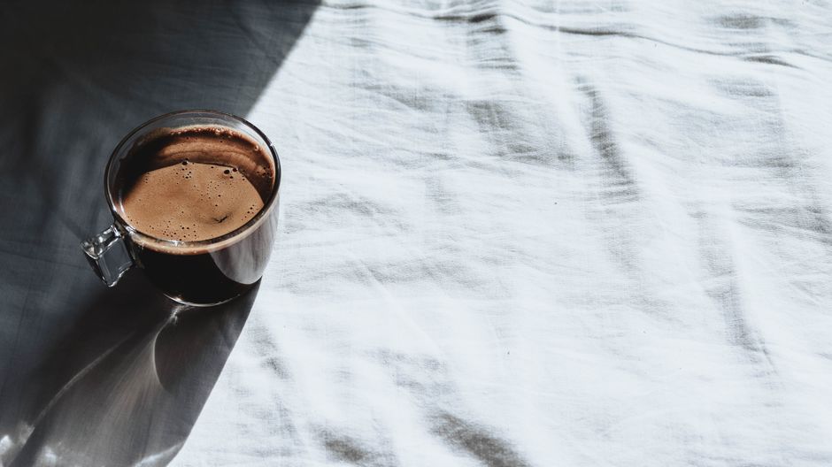 Glass cup of coffee casting shadows on a bright white sheet in natural sunlight.