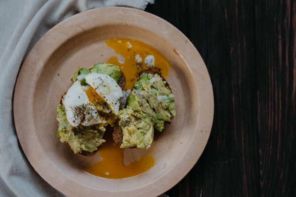 Mouthwatering avocado toast topped with a perfectly poached egg on a ceramic plate.