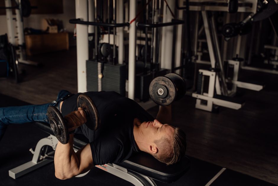 Muscular man doing dumbbell chest press exercise in a gym setting, highlighting fitness and strength.