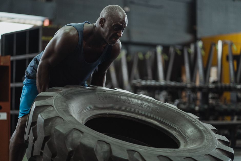 Muscular man performing tire flip exercise in a gym, showcasing strength and determination.