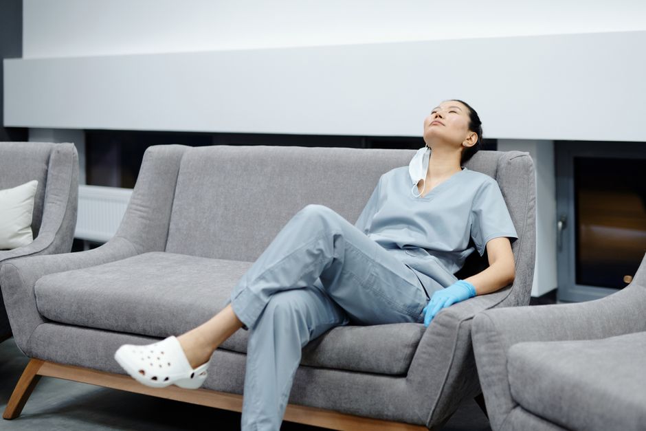 Nurse in scrubs takes a break, resting on a comfy hospital couch after a long shift.