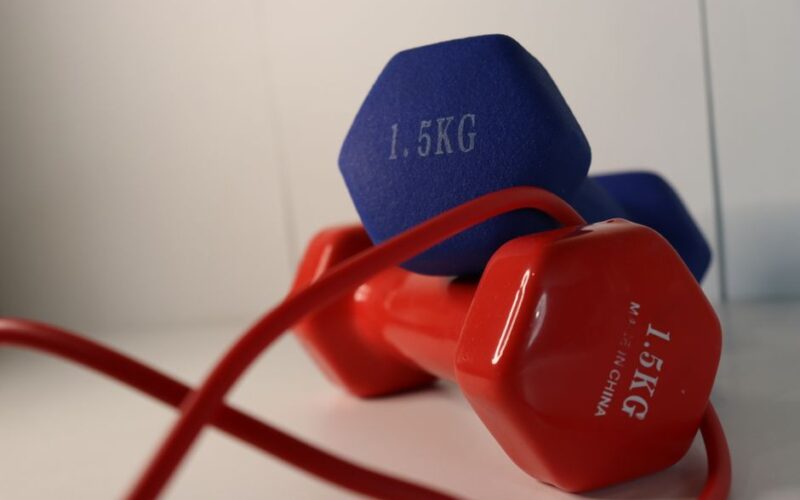 Pair of vibrant dumbbells with a red skipping rope on a white surface, perfect for home workouts.