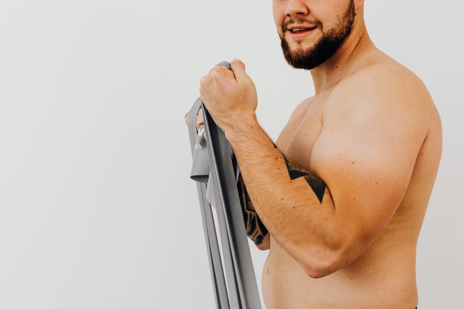 Shirtless man using resistance band for strength training indoors.