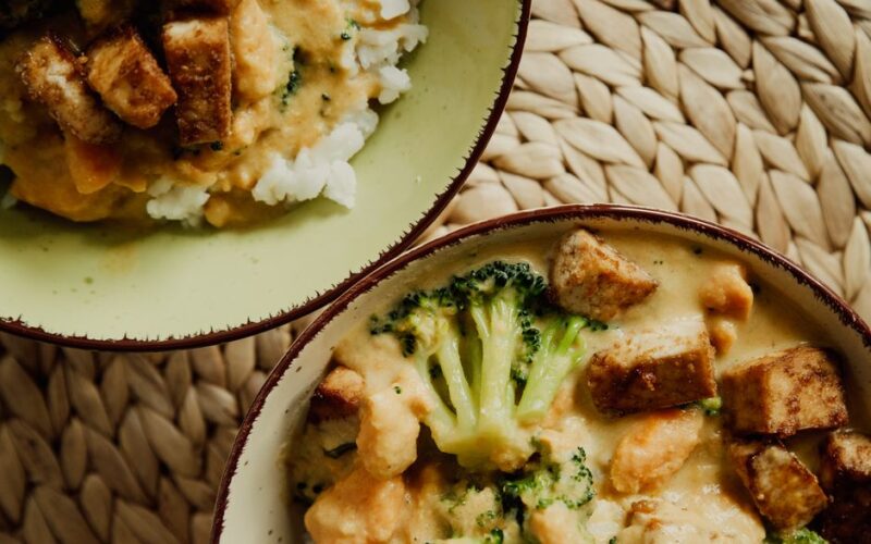 Tasty vegan bowl with broccoli, tofu, and creamy sauce served on a woven mat.