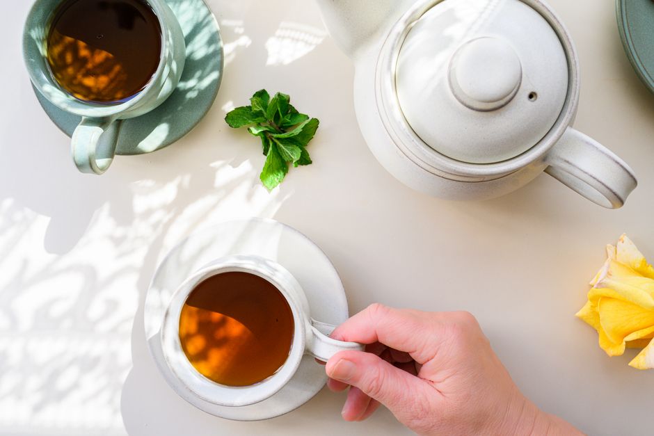 Top view of a serene tea setup with a hand holding a cup, accompanied by a teapot and fresh mint.