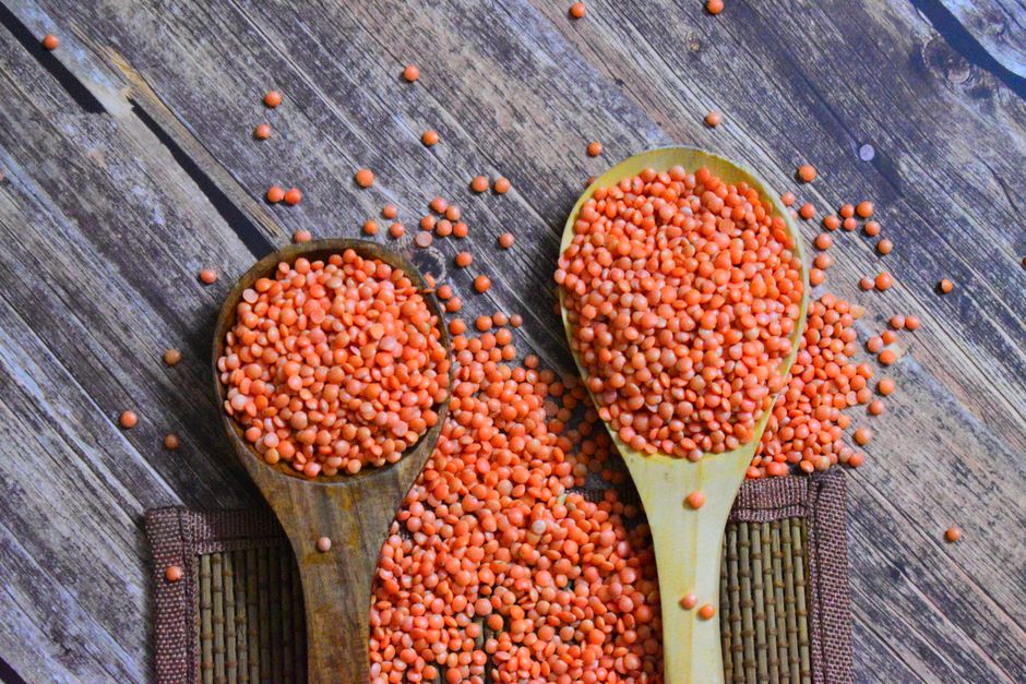 Two wooden spoons filled with vibrant red lentils on a rustic wooden surface.