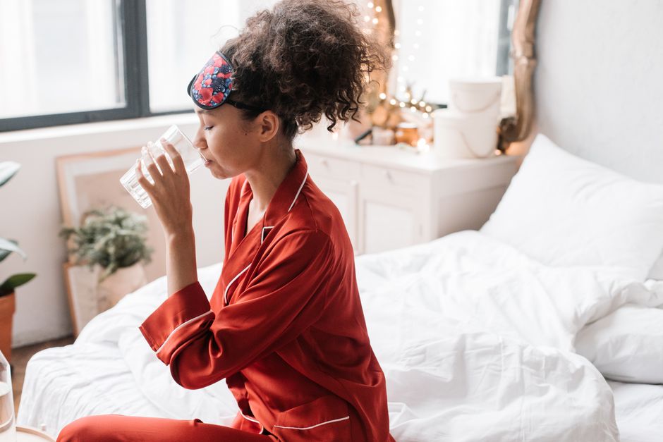 Woman in red pajamas drinking water, enhancing morning wellness rituals.